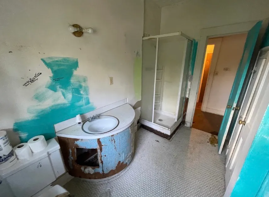 Bathroom before remodeling, with a damaged vanity, patchy teal paint, and worn fixtures