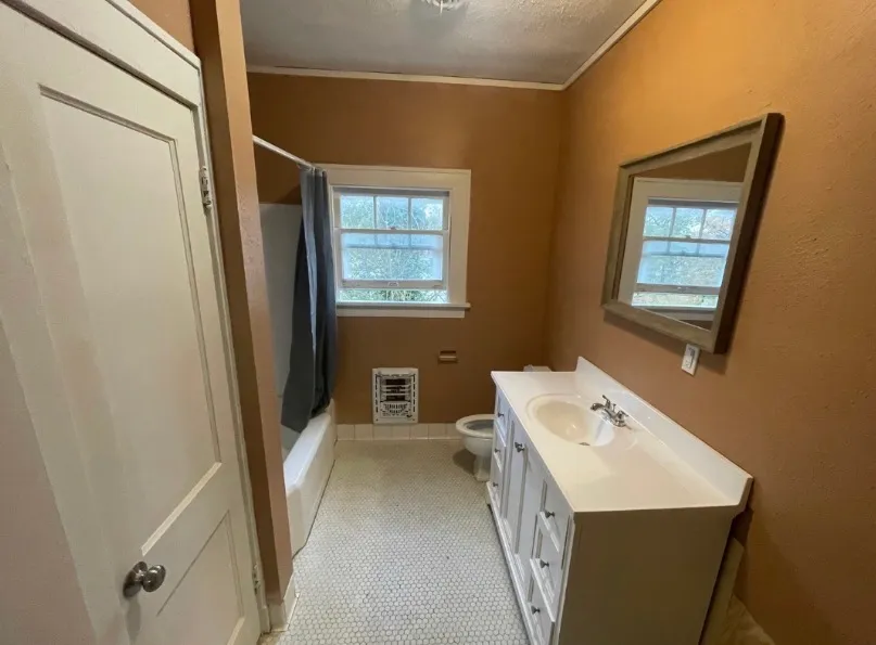The same bathroom after remodeling, with fresh warm paint, a new white vanity, framed mirror, and clean tub surround