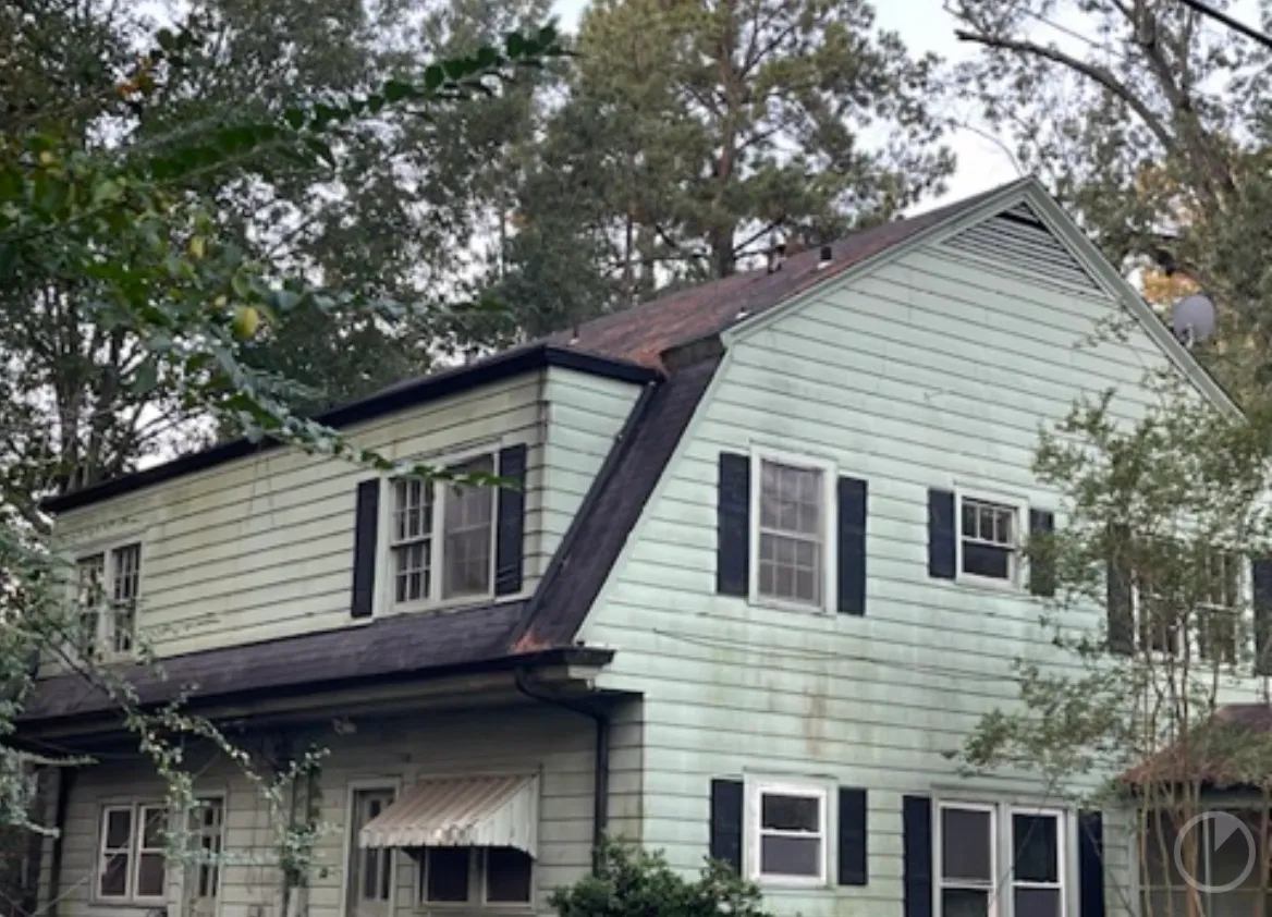 Two-story home before exterior work, with faded, weathered pale-green siding and a worn, rusted brown roof