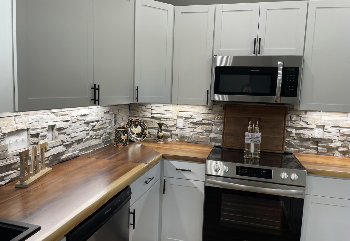 Kitchen remodel with white shaker cabinets, a butcher-block wood countertop, stacked-stone backsplash, and stainless microwave and range