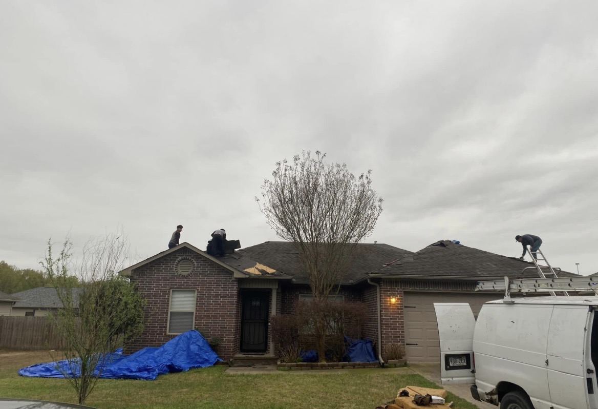 Roof replacement in progress on a brick home, with the crew tearing off old shingles and protective tarps around the house