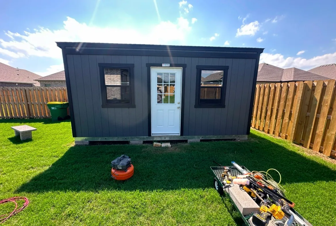 Charcoal-gray manufactured shed on install day, before customization, with tools and equipment still on site and an open base